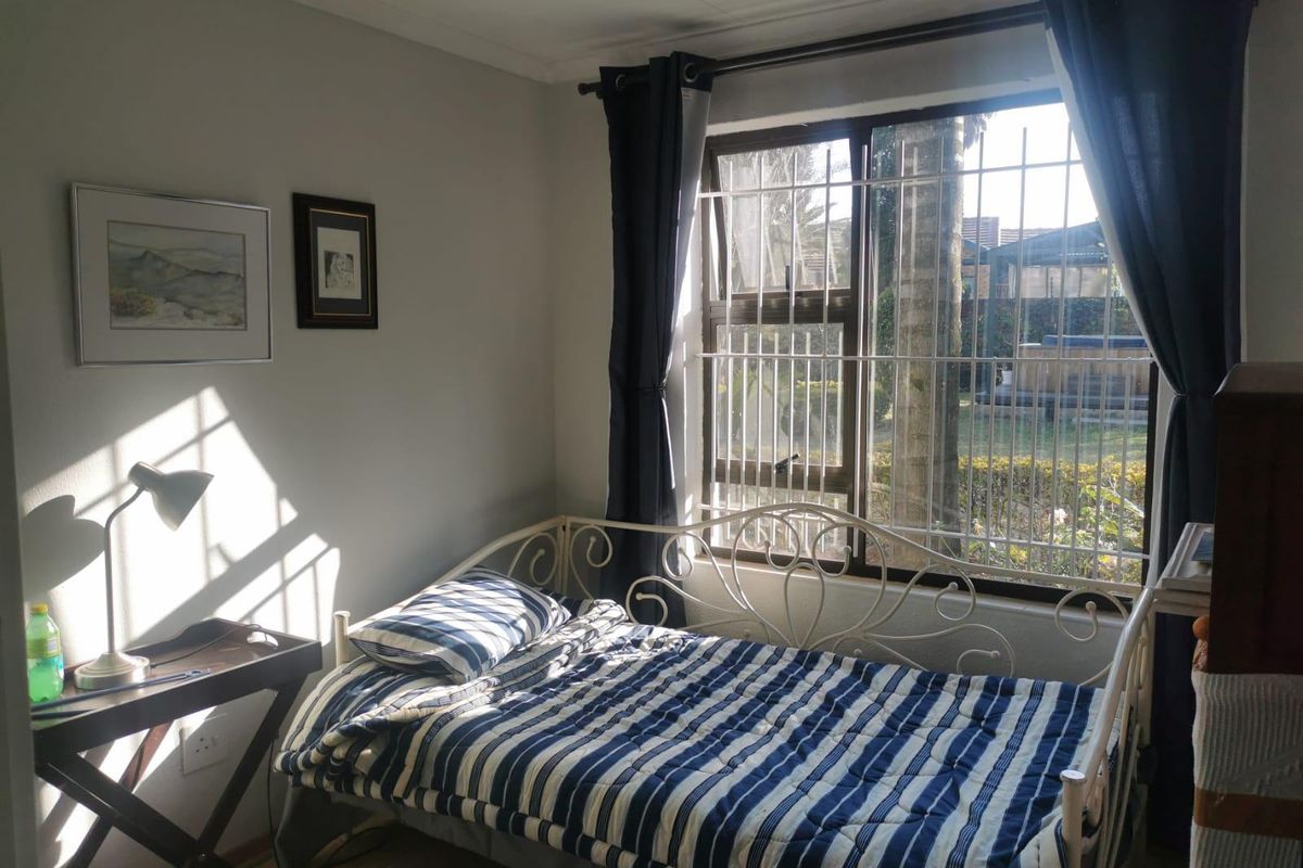 A bedroom featuring laminate flooring and a window fitted with security bars, allowing natural light into the space.