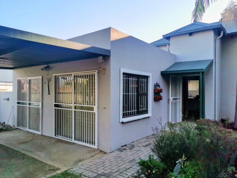Front elevation of the house featuring a covered carport, secure metal gates, and a paved walkway leading to the entrance.