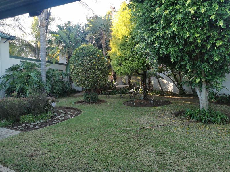 A well-maintained private garden featuring mature trees, established landscaping, and a paved walkway, providing a peaceful outdoor space.