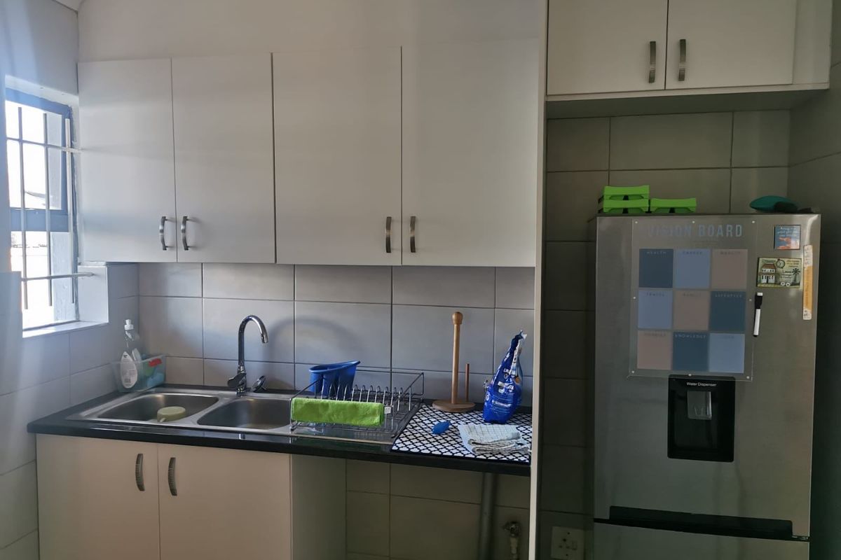 A functional kitchen area featuring white built-in cabinetry, a double basin sink with mixer tap, and tiled splashbacks.