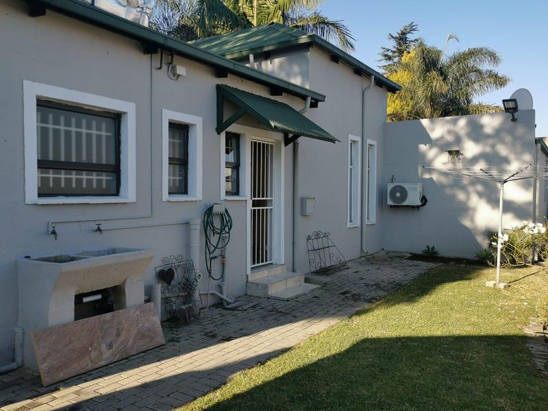 Rear exterior view of the property featuring a paved walkway, concrete laundry trough, security gate, and wall-mounted air conditioning unit.