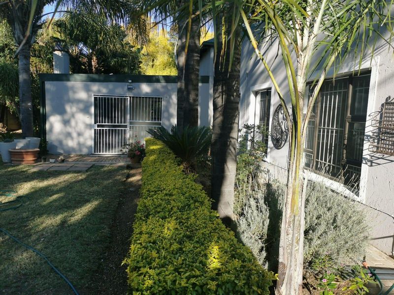 A view of the rear exterior of the house featuring a landscaped garden, paved pathways, and security-fitted windows and doors.