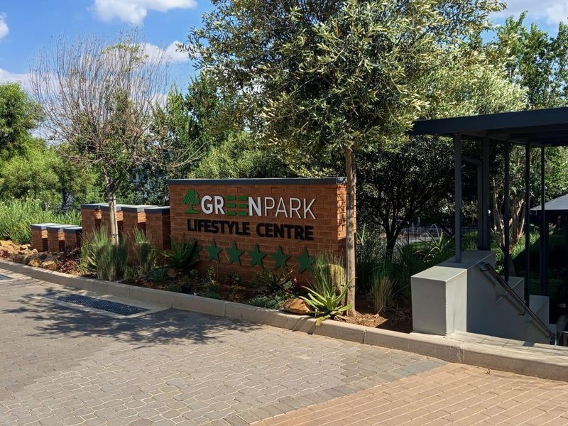 Entrance view of the Greenpark Lifestyle Centre featuring a brick signage wall, paved driveway, and landscaped garden area.