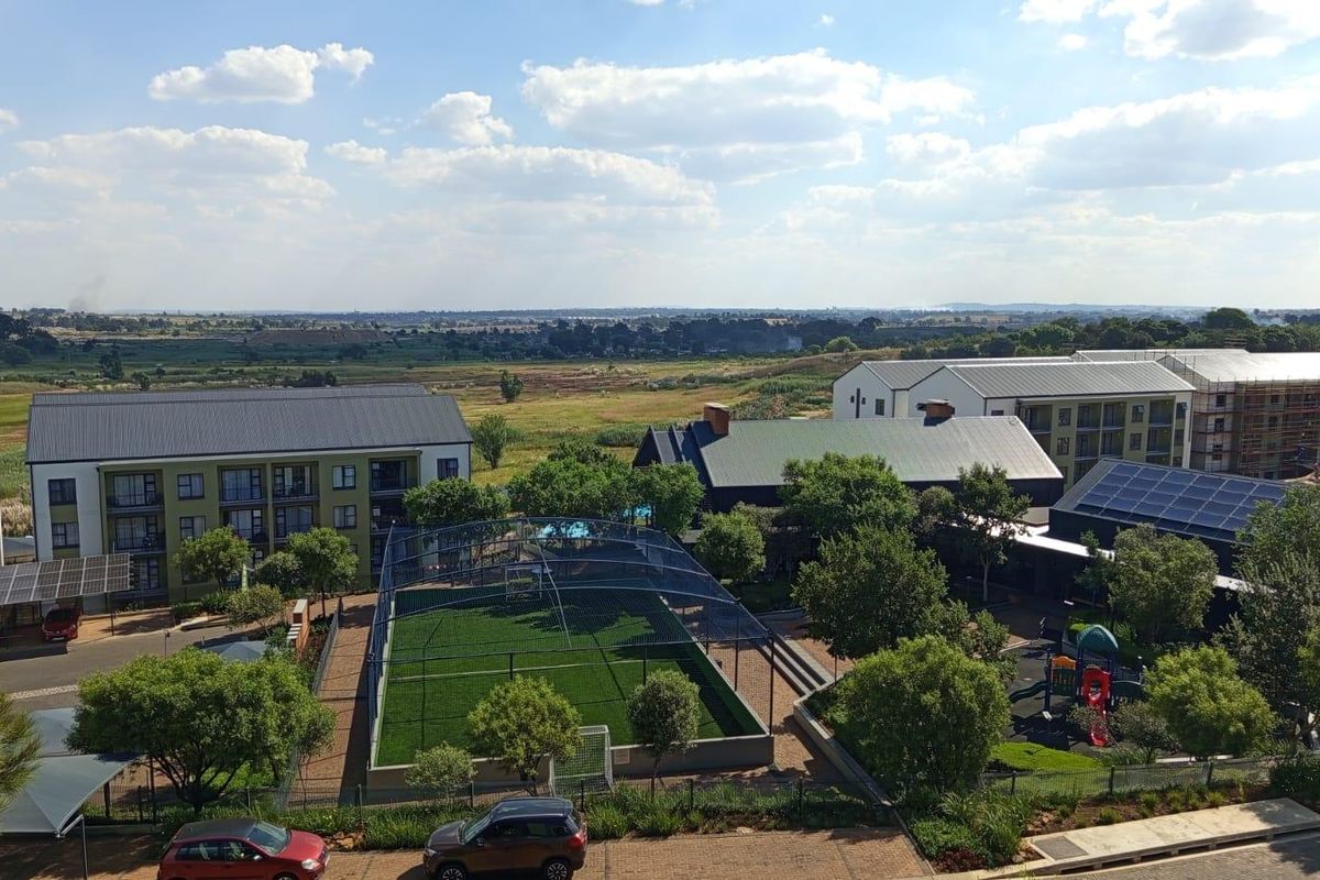 Aerial view of the apartment complex grounds, featuring a sports court, playground, landscaped gardens, and solar-equipped building roofs.