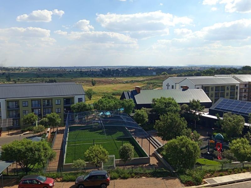 Aerial view of the apartment complex grounds, featuring a sports court, playground, landscaped gardens, and solar-equipped building roofs.