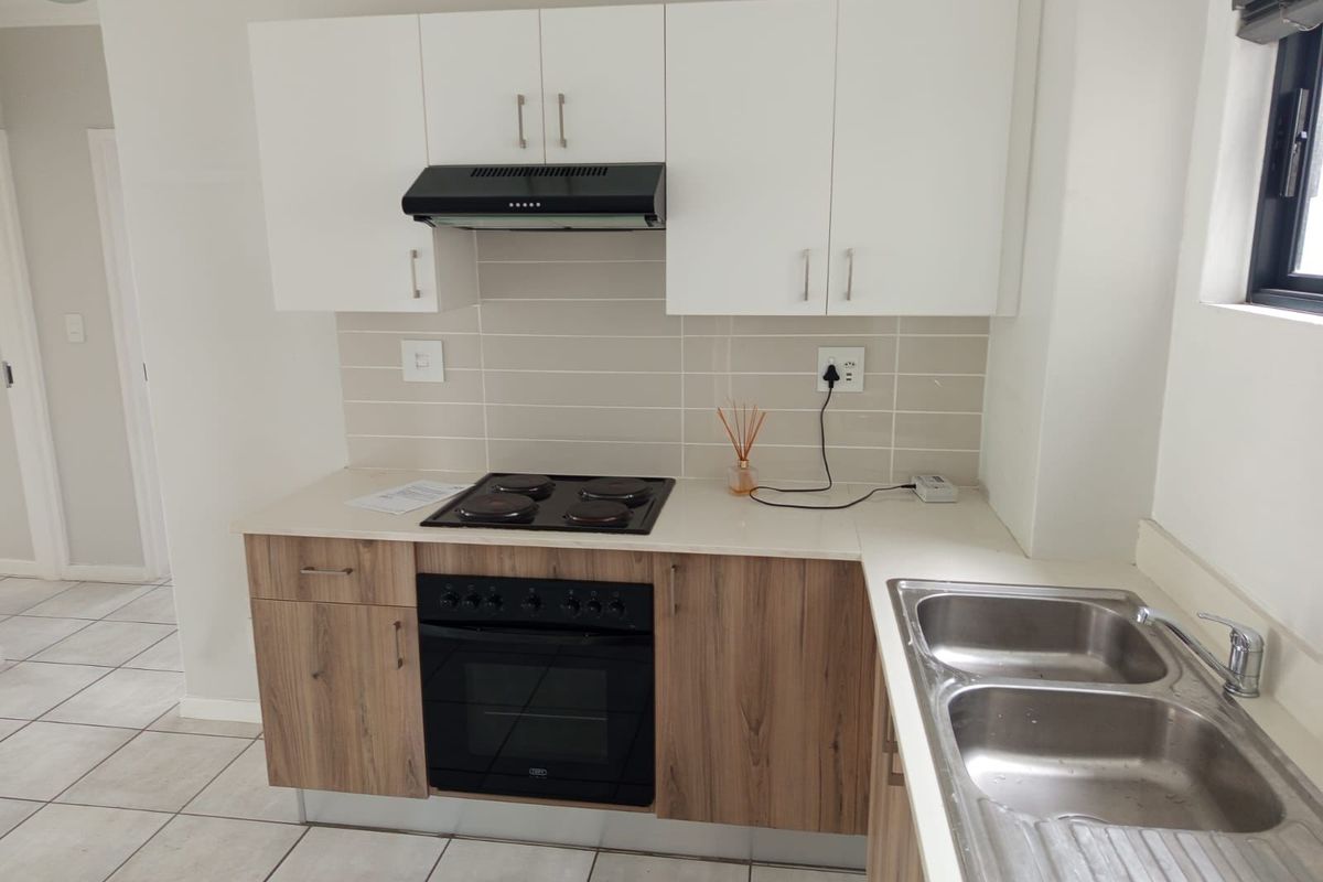 A clean, modern kitchen featuring white upper cabinets, wood-finish lower cabinetry, a built-in oven, electric hob, and a double stainless steel sink.