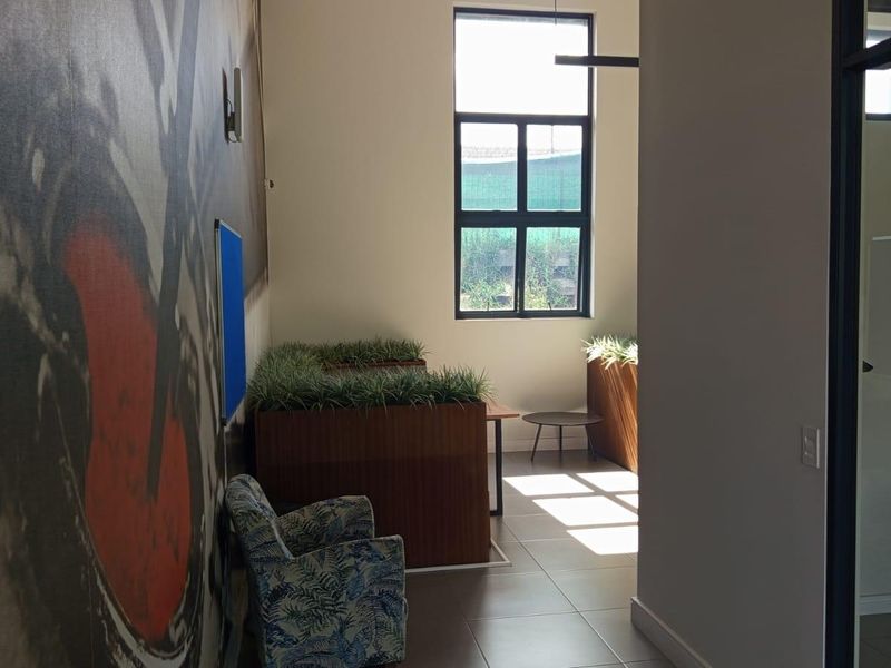 A bright office space featuring large windows, tiled flooring, and integrated built-in planters, offering a functional and modern workspace environment.