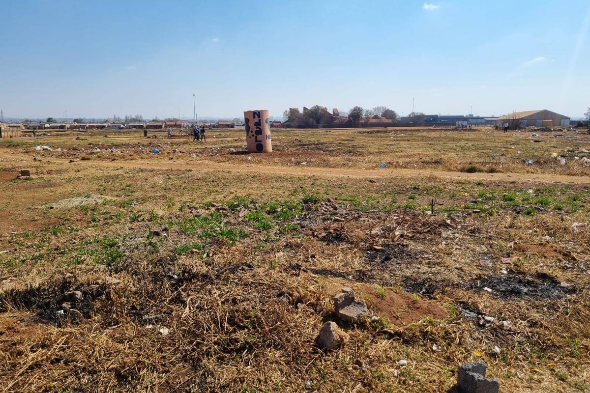 A wide-angle view of a vacant residential plot featuring dry grass and open space, suitable for future development.