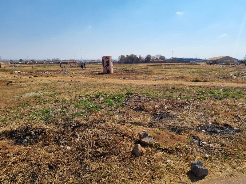 A wide-angle view of a vacant residential plot featuring dry grass and open space, suitable for future development.
