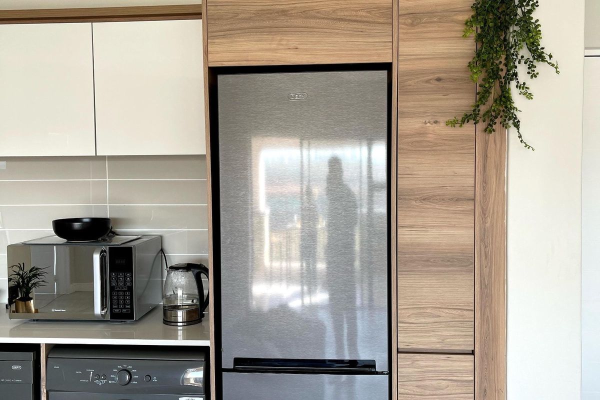 Modern kitchen area featuring sleek white and wood-grain cabinetry, tiled backsplash, and integrated appliance housing.