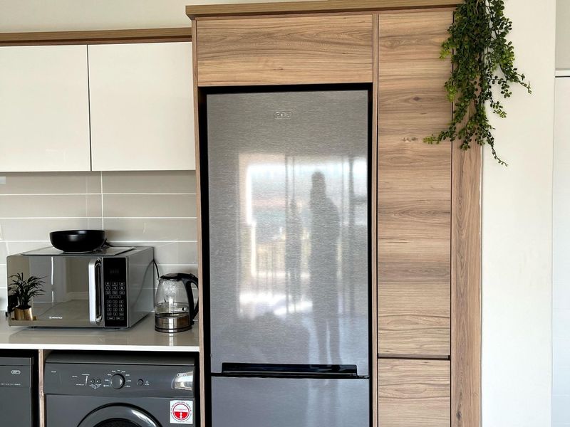 Modern kitchen area featuring sleek white and wood-grain cabinetry, tiled backsplash, and integrated appliance housing.