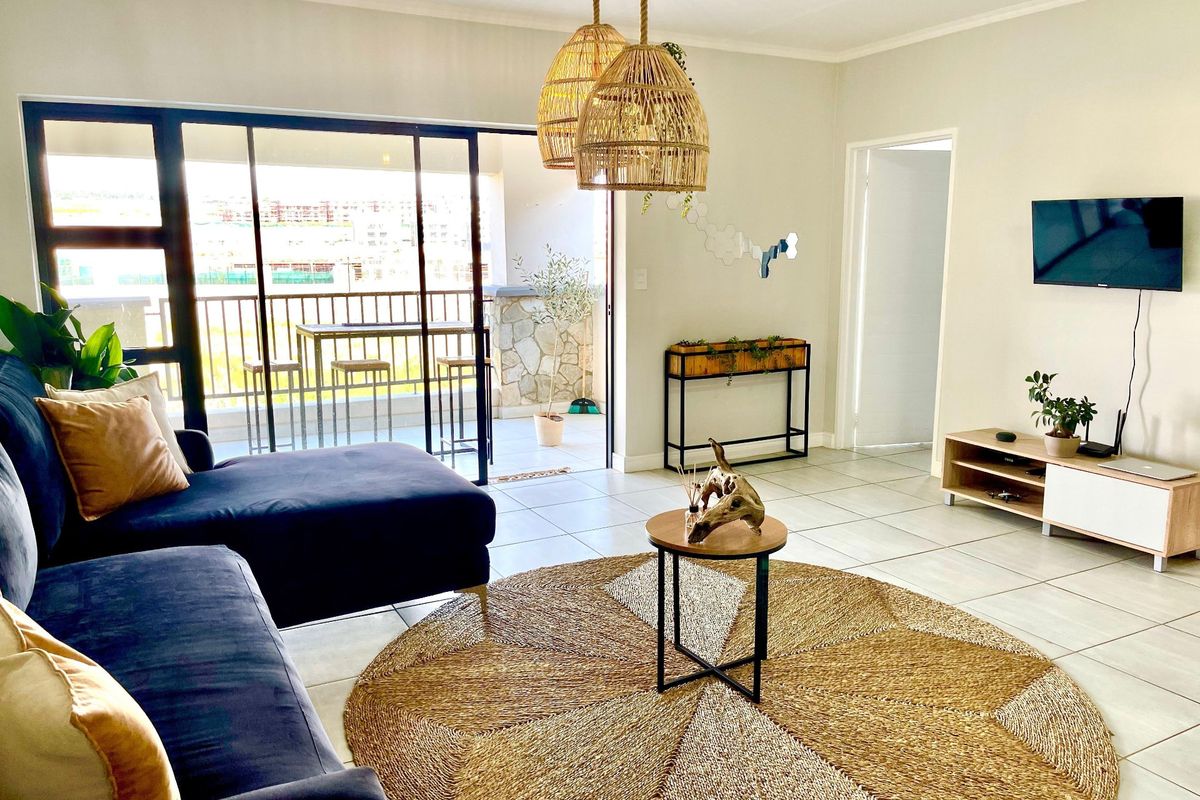 Bright and airy living room featuring large sliding glass doors that open onto a private balcony, complemented by neutral tiled flooring.
