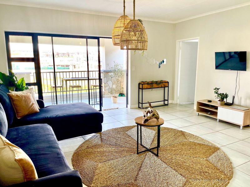 Bright and airy living room featuring large sliding glass doors that open onto a private balcony, complemented by neutral tiled flooring.