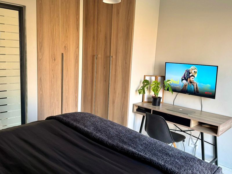 A well-maintained bedroom featuring modern wood-finish built-in cupboards and a sliding door providing natural light.