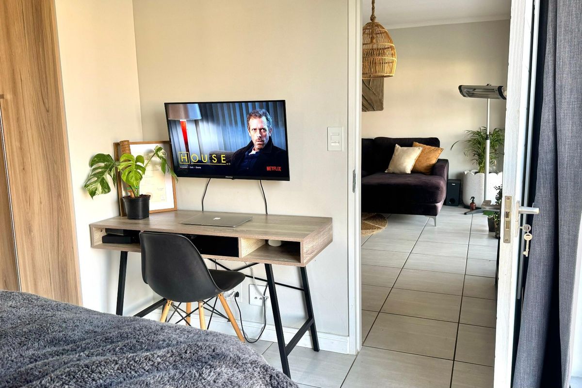 Bedroom featuring built-in wardrobes and tiled flooring, with a direct view into the adjacent living area through an open doorway.