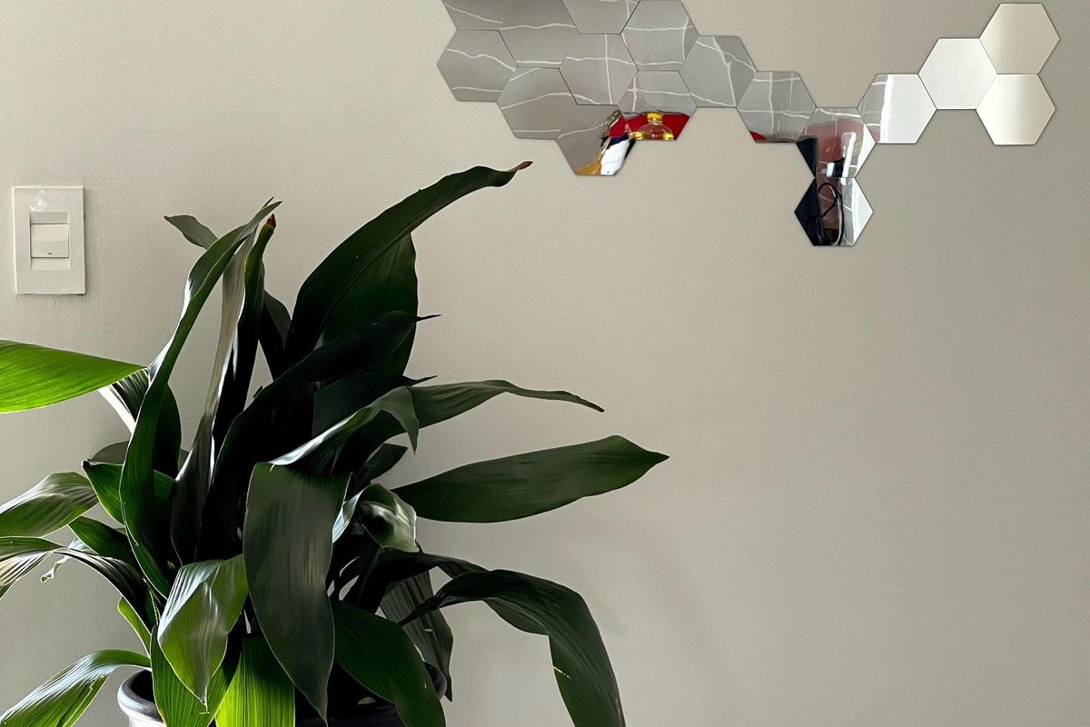 A close-up view of a plain interior wall featuring a decorative hexagonal mirror arrangement and a light switch.