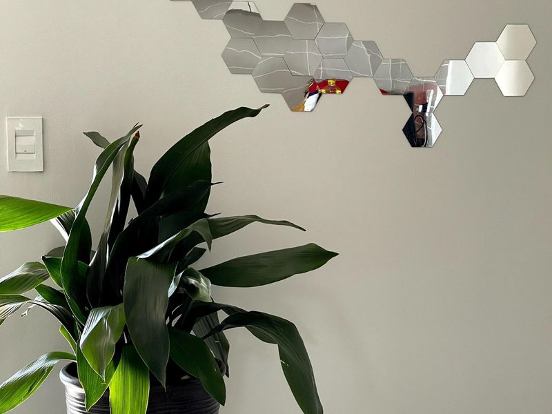 A close-up view of a plain interior wall featuring a decorative hexagonal mirror arrangement and a light switch.