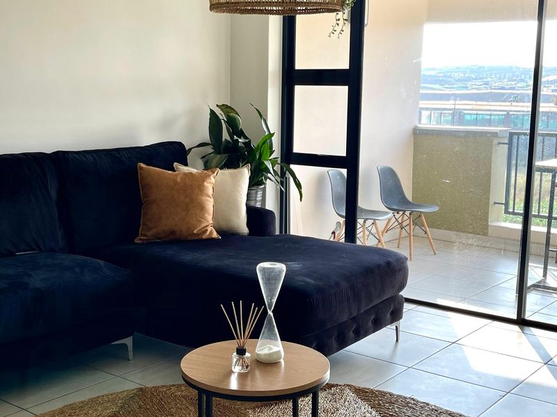 A bright living room featuring tiled flooring and large sliding glass doors that provide seamless access to an outdoor balcony area.