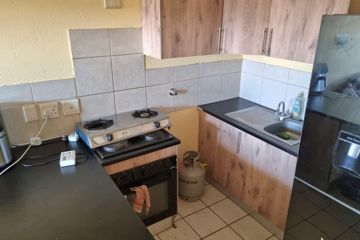 Compact kitchen featuring wood-look cabinetry, dark laminate countertops, a gas hob, built-in oven, and tiled backsplash with floor tiling.