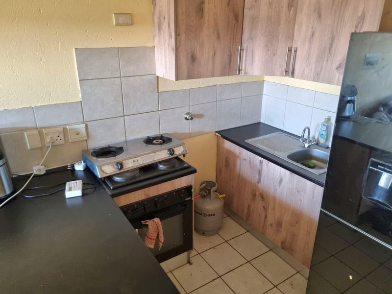 Compact kitchen featuring wood-look cabinetry, dark laminate countertops, a gas hob, built-in oven, and tiled backsplash with floor tiling.