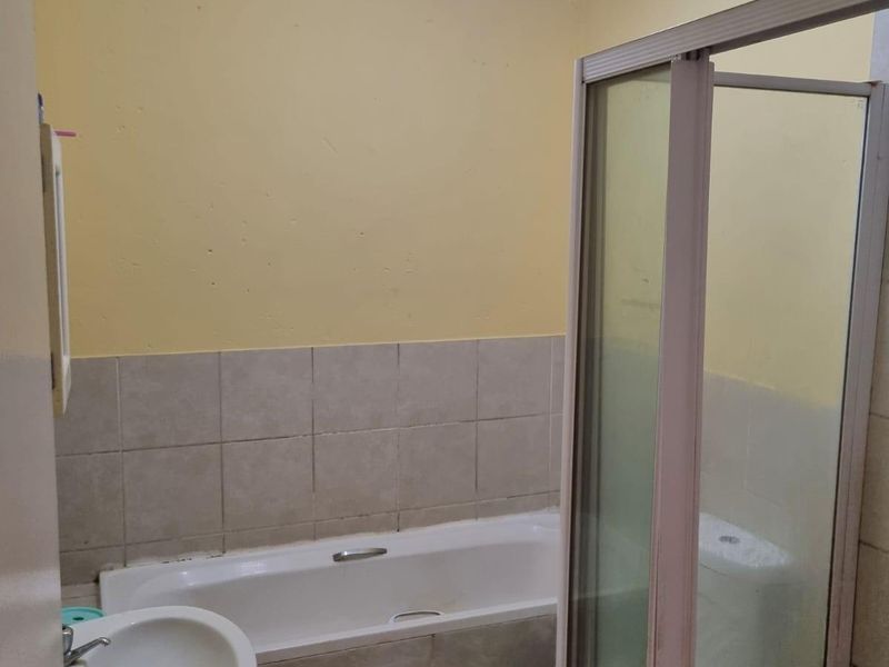 A functional bathroom featuring a pedestal basin, built-in bathtub, and a separate shower enclosure with tiled finishes.