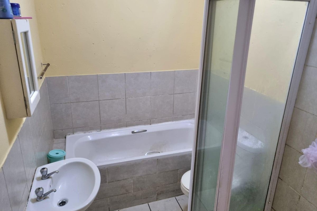 A functional bathroom featuring a bathtub, separate shower enclosure, and pedestal basin with tiled finishes, requiring cosmetic updates to improve its overall condition.