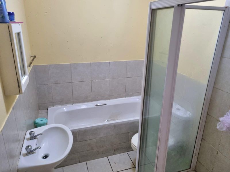 A functional bathroom featuring a bathtub, separate shower enclosure, and pedestal basin with tiled finishes, requiring cosmetic updates to improve its overall condition.