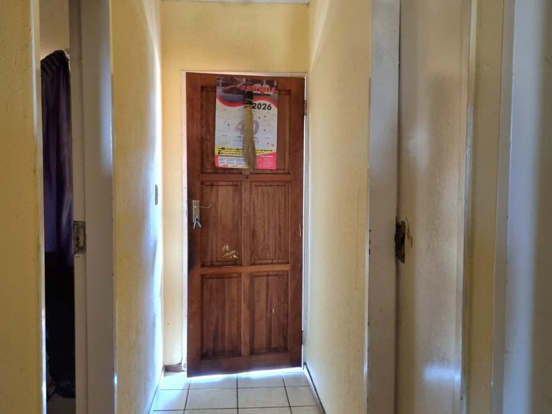 A functional hallway featuring tiled flooring and access to adjacent rooms, requiring cosmetic updates to the walls and doors.