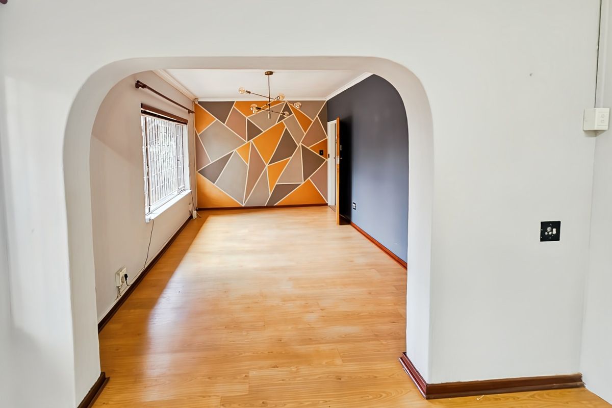An empty living room featuring laminate flooring, a decorative archway entrance, and a geometric accent wall with a modern ceiling light fixture.