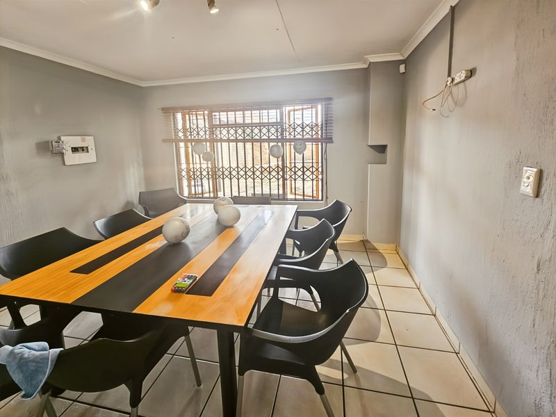 A functional dining area featuring tiled flooring, security window gates, and neutral wall finishes, suitable for a commercial office or meeting space.