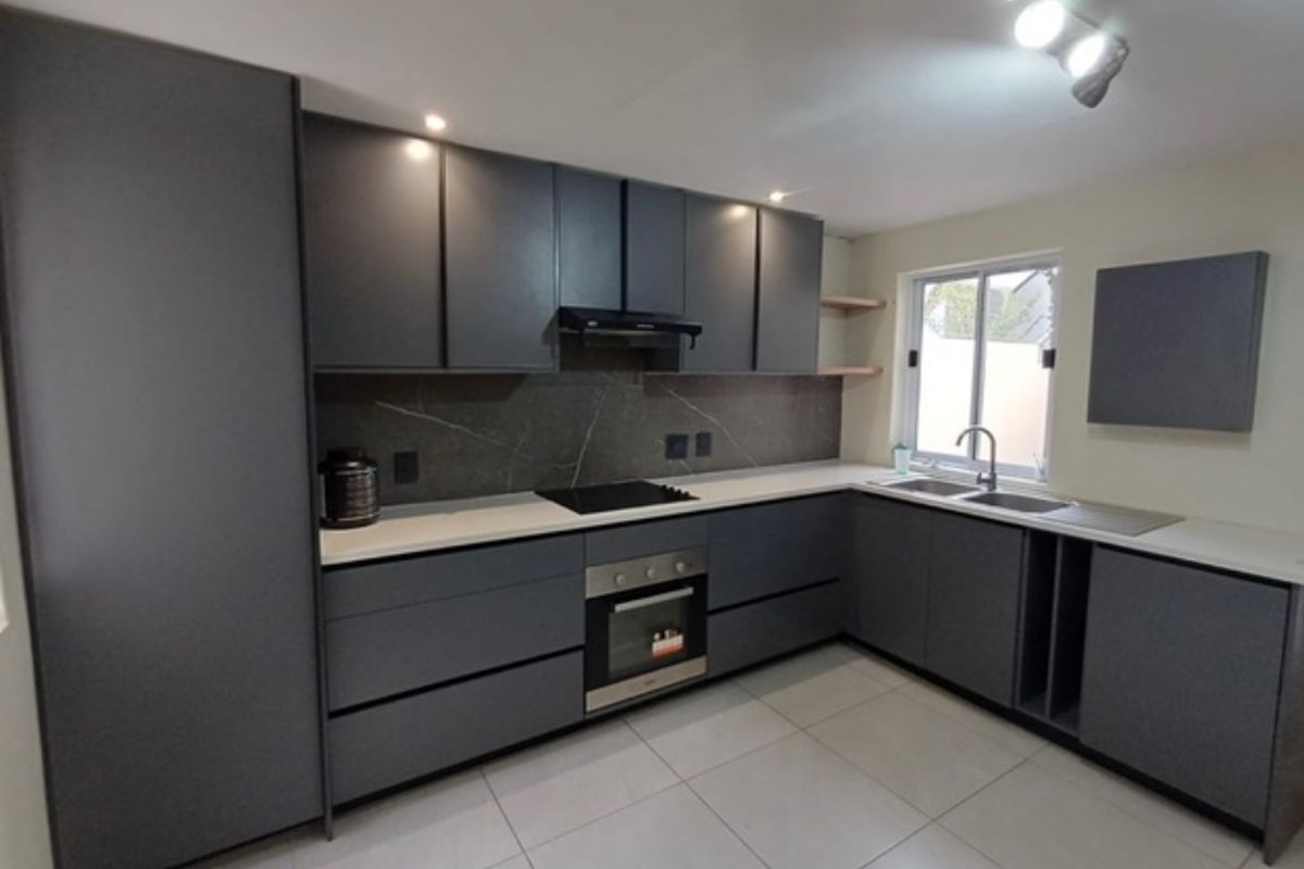 Modern kitchen featuring dark grey cabinetry, stone countertops, integrated appliances, and tiled flooring in a clean, contemporary layout.