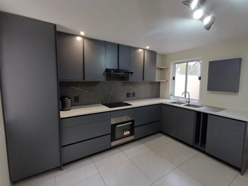 Modern kitchen featuring dark grey cabinetry, stone countertops, integrated appliances, and tiled flooring in a clean, contemporary layout.