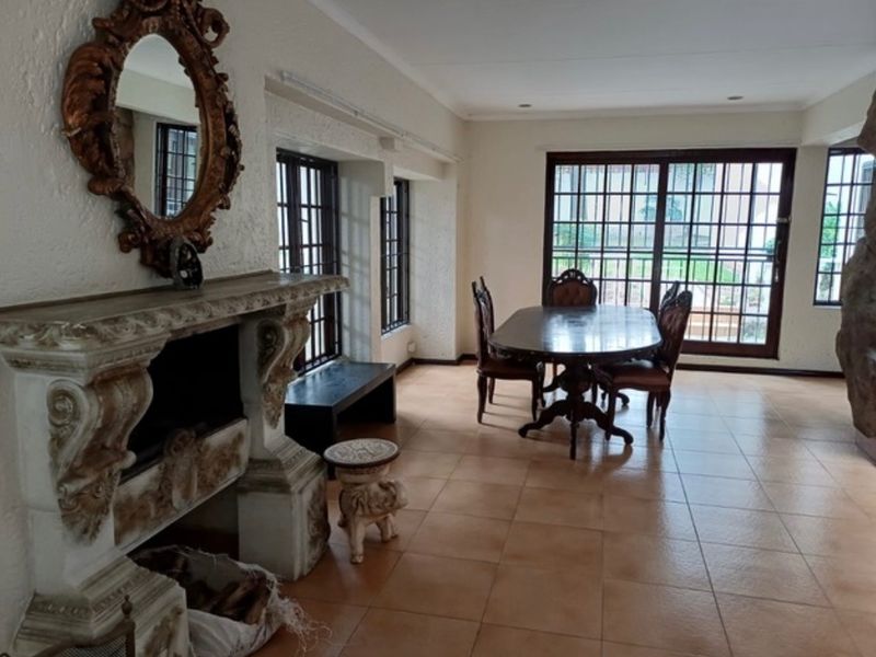 Spacious dining area featuring an ornate stone fireplace, tiled flooring, and large glass sliding doors providing access to the exterior.