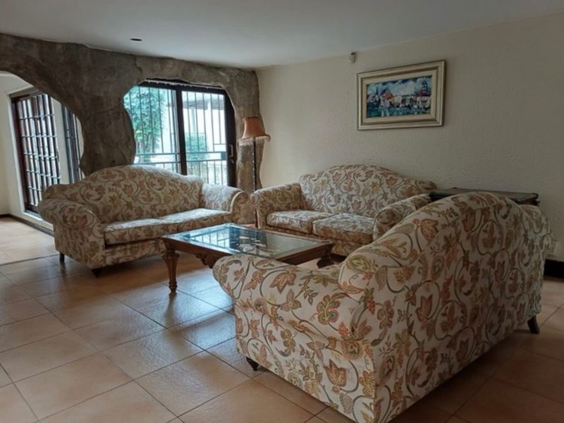 A living room featuring tiled flooring and a unique decorative rock feature wall surrounding the sliding glass doors with security bars.