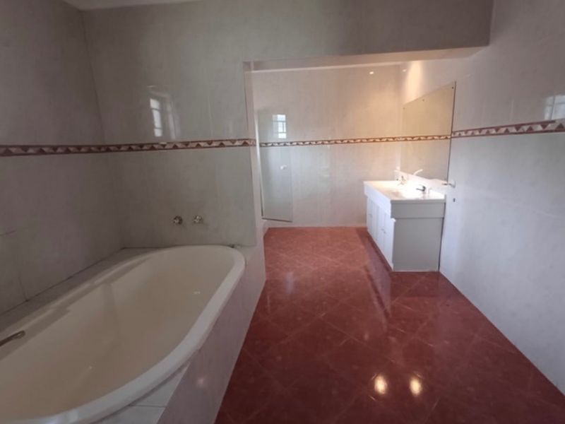A spacious, empty bathroom featuring a built-in bathtub, a vanity cabinet with a mirror, and tiled flooring.