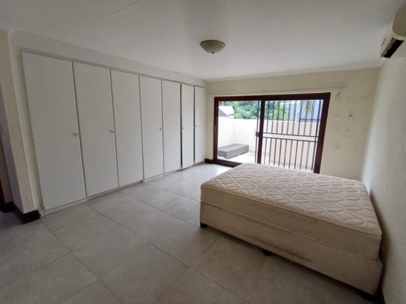 Bedroom featuring extensive built-in cupboards, tiled flooring, and a sliding door leading to an outdoor area, equipped with a wall-mounted air conditioning unit.