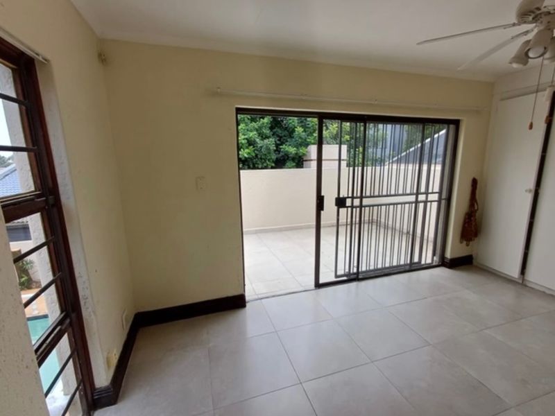 An empty living room featuring tiled flooring, a ceiling fan, and a sliding glass door providing access to an outdoor patio area.