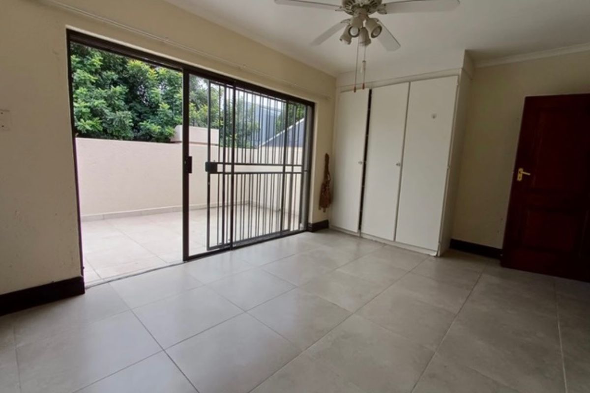 A spacious bedroom featuring tiled flooring, built-in cupboards, a ceiling fan, and direct access to an outdoor patio through a sliding glass door.