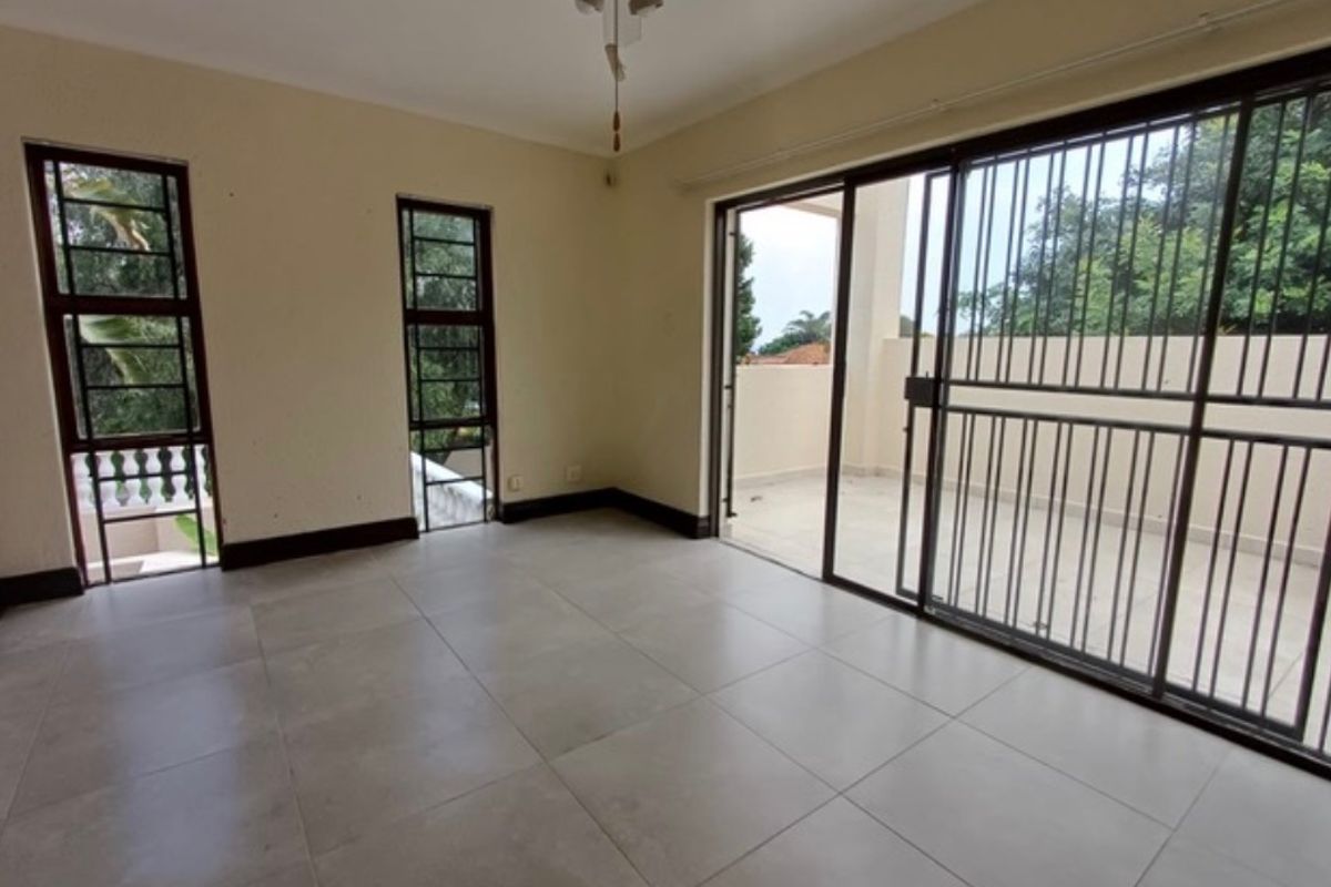 Spacious, empty living area featuring large tiled floors, a ceiling fan, and sliding glass doors that open onto an outdoor patio space.