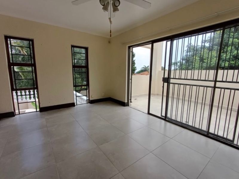 Spacious, empty living area featuring large tiled floors, a ceiling fan, and sliding glass doors that open onto an outdoor patio space.