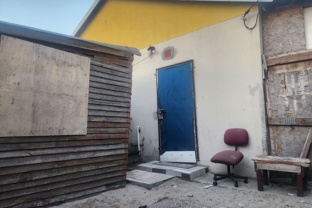 Rear exterior view of the property showing a weathered building facade, a damaged door, and basic structural elements in need of maintenance.