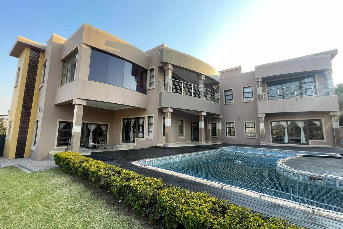 A spacious rear exterior view of a modern double-story house featuring a swimming pool, timber decking, and upper-level balconies with stainless steel railings.