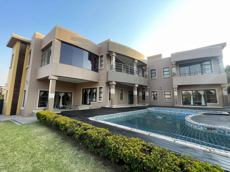 A spacious rear exterior view of a modern double-story house featuring a swimming pool, timber decking, and upper-level balconies with stainless steel railings.