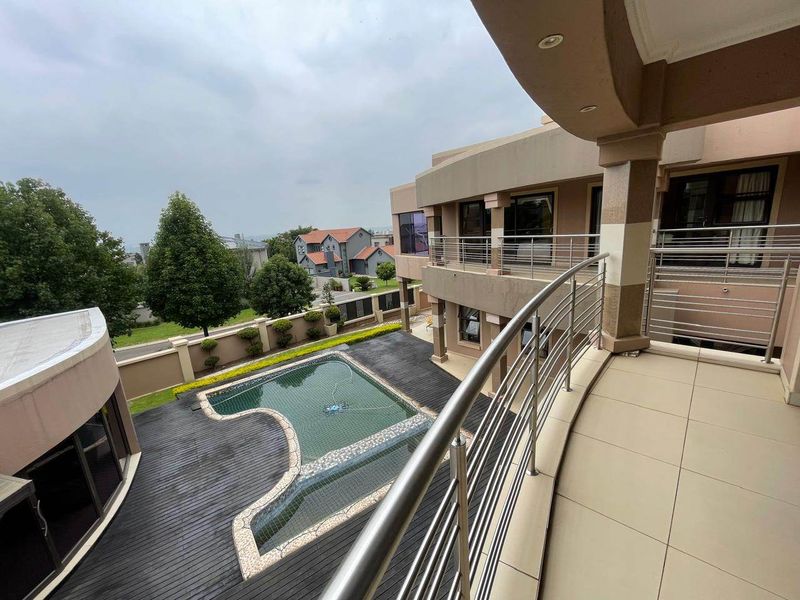 Spacious upper-level balcony featuring stainless steel balustrades, overlooking a private swimming pool area with timber decking and landscaped garden surroundings.