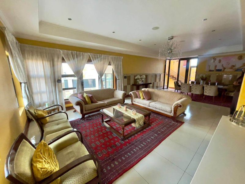 Spacious open-plan living and dining area featuring tiled floors, recessed lighting, a crystal chandelier, and large sliding glass doors providing natural light.