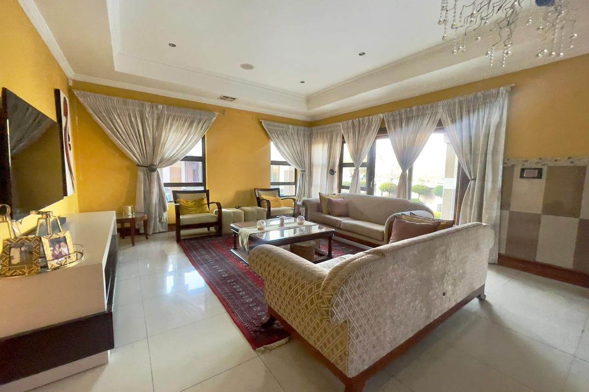 Spacious living room featuring a tray ceiling, recessed lighting, a crystal chandelier, and large windows that provide ample natural light.