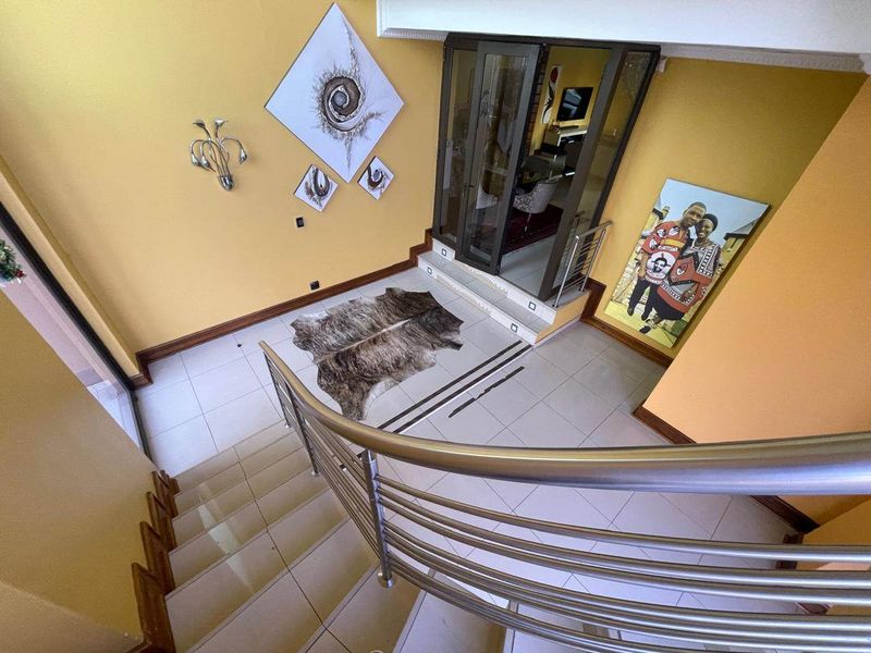 Spacious entrance foyer featuring a curved staircase with a modern stainless steel balustrade and tiled flooring leading to glass-panelled double doors.