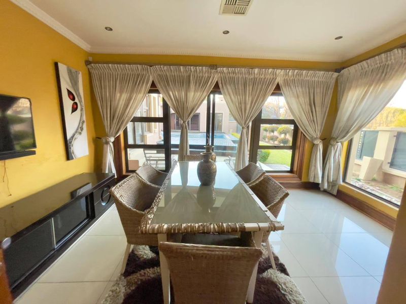 A bright dining room featuring large windows, tiled flooring, and direct access to the outdoor pool area through sliding glass doors.