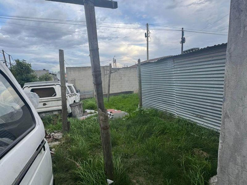 Rear outdoor area featuring corrugated metal fencing and an overgrown yard with a leaning utility pole.