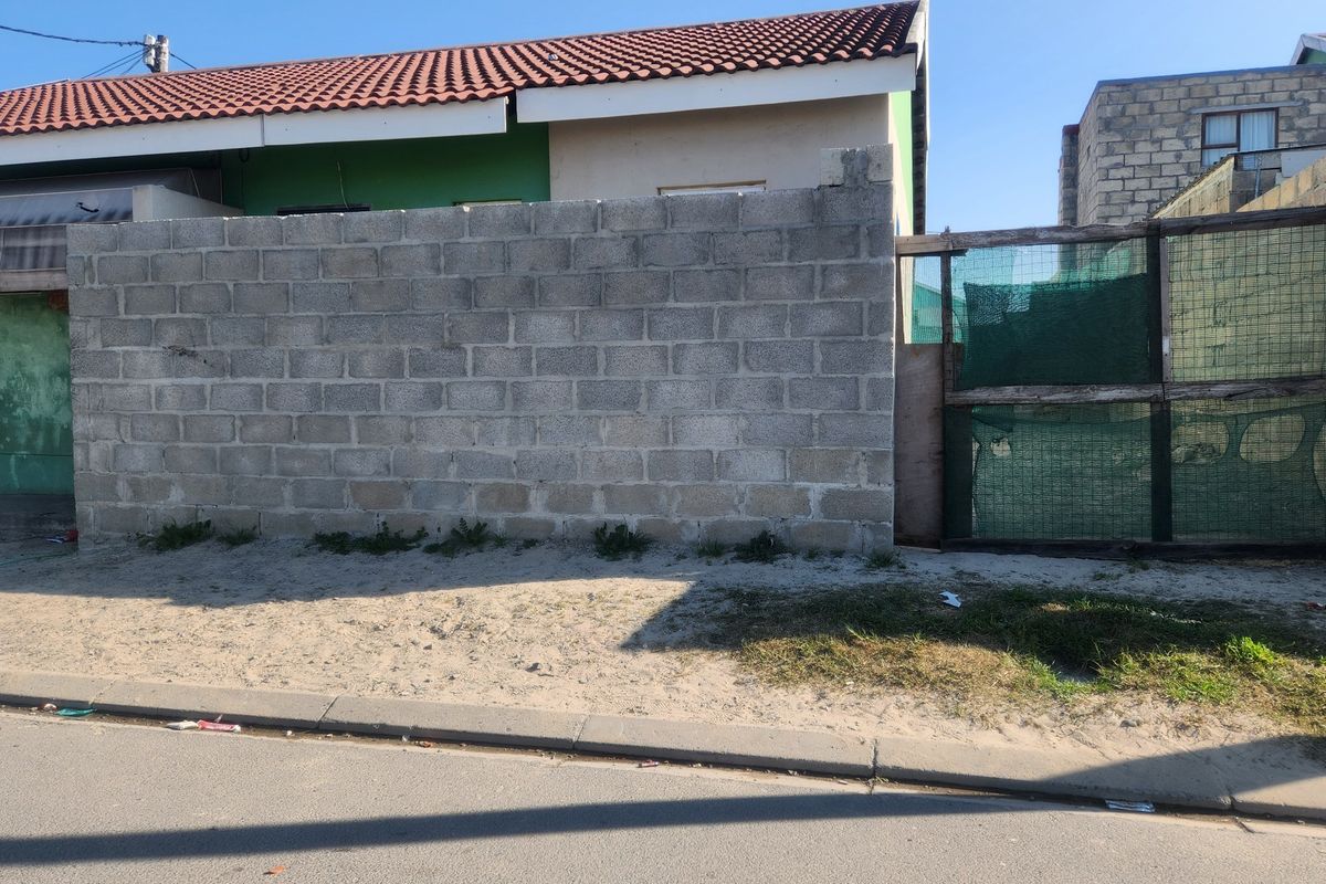 Front view of the property featuring a concrete block boundary wall, mesh gate, and tiled roof structure.
